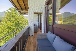 A balcony with a wooden floor, a cushioned seating area, and a view of a mountainous landscape. - Premium Lake view Suite | Adults only (Strobl)