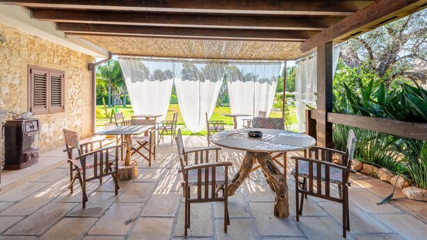 Un patio al aire libre con mesas y sillas de madera, un muro de piedra y vistas al follaje.