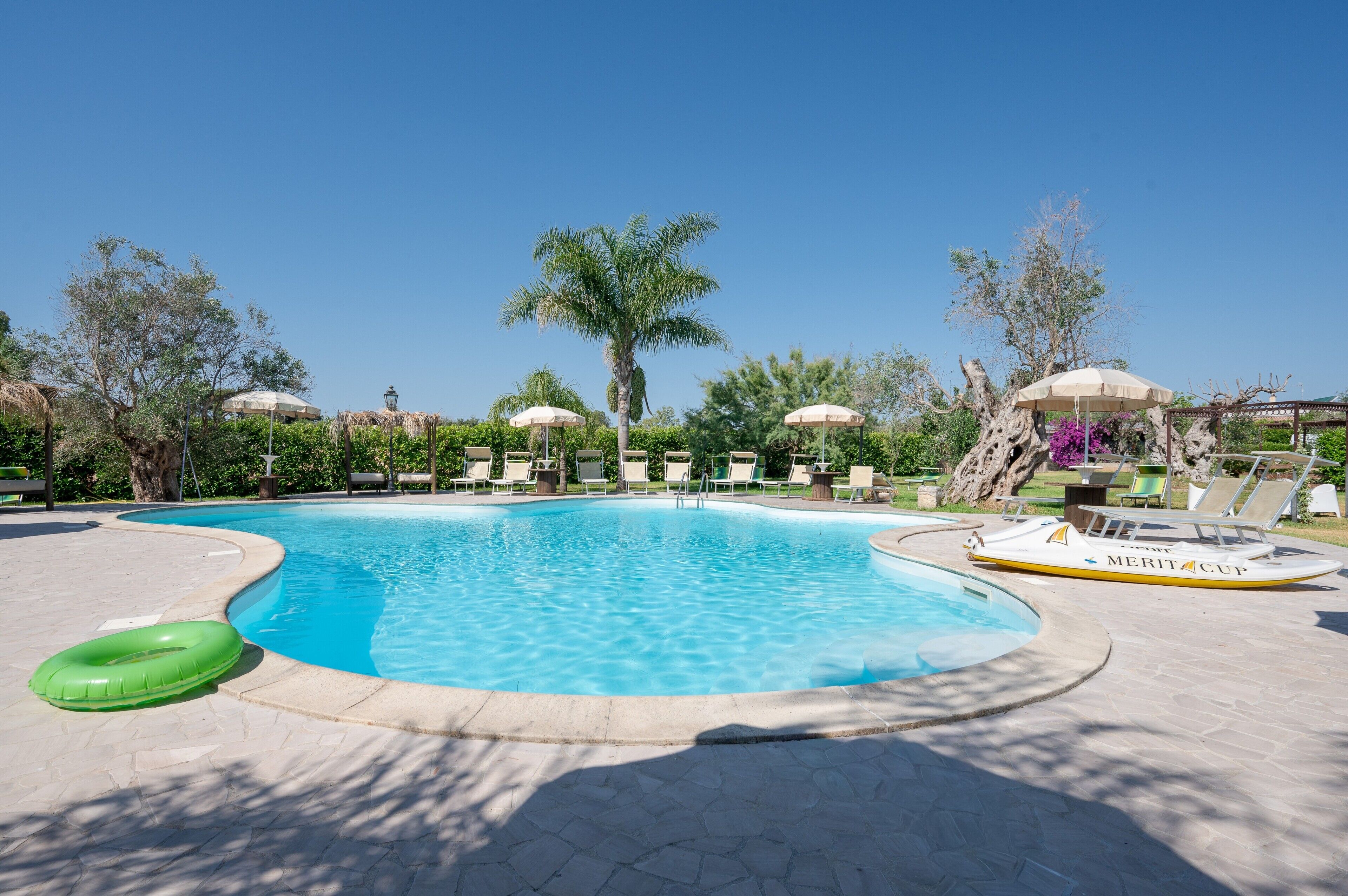 A swimming pool with lounge chairs and umbrellas, surrounded by trees and a palm tree.