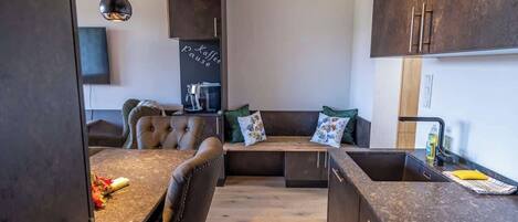 A modern kitchen with a built-in coffee machine, a dining area with a bench, and a large cabinet.
