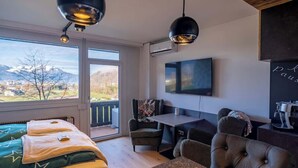 Una habitación con cama, una mesa, un televisor y vistas a las montañas.