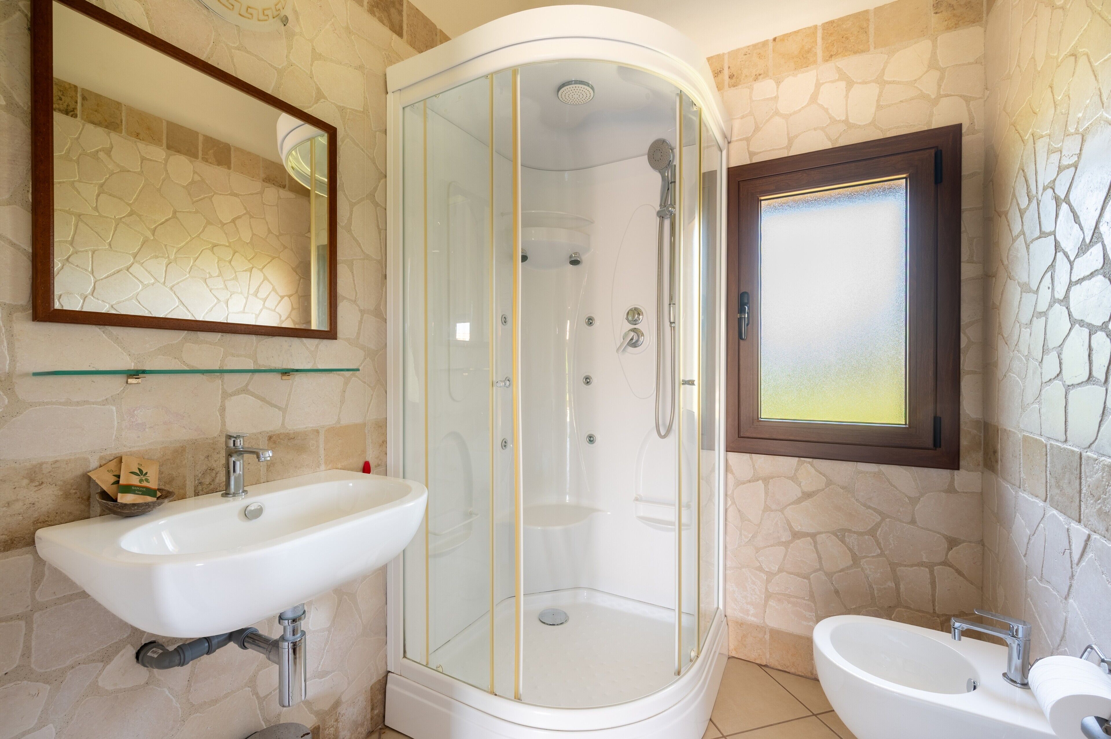Een badkamer met een douchecabine van glas, een witte wastafel en een spiegel.