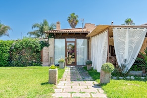 Uma casa com um caminho de pedra que leva a uma porta de madeira, rodeada por vegetação e um céu claro.