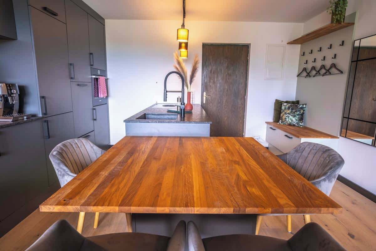 Eine moderne Küche mit einem Holztisch, grauen Schränken und einer hängenden Pendelleuchte.
