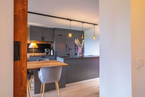 Eine moderne Küche mit Esstisch aus Holz, grauen Schränken, Pendelleuchten und einer kleinen Kücheninsel.