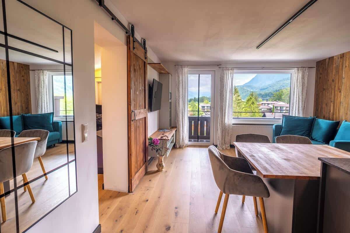 Une pièce moderne avec un plancher en bois, une table à manger avec des chaises, un canapé, un téléviseur fixé à un mur en bois et une grande fenêtre donnant sur les montagnes.