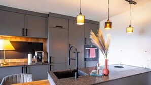 Una cocina moderna con armarios oscuros, encimera de granito, un lavabo, una cafetera y luces colgantes.