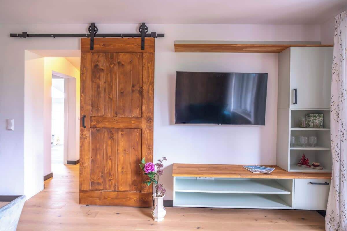 Un salon doté d’une porte coulissante de style rustique, d’un téléviseur fixé au mur, d’un banc en bois et d’un meuble blanc avec des étagères.