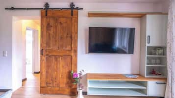 Un salon doté d’une porte coulissante de style rustique, d’un téléviseur fixé au mur, d’un banc en bois et d’un meuble blanc avec des étagères.