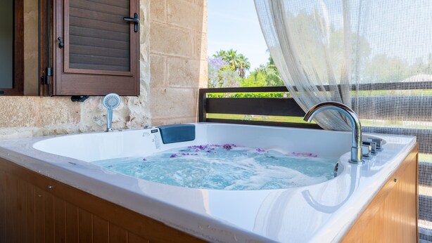 Un jacuzzi con indicador de temperatura, un banco de madera y vistas a follaje a través de una ventana.