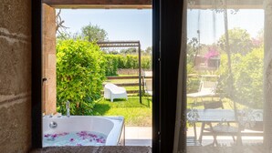 Vista desde una ventana que muestra un jardín con jacuzzi, una pérgola de madera y mobiliario exterior.