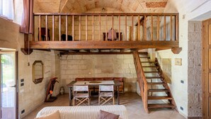 Una habitación rústica con cama entrepiso, una mesa de comedor con sillas, una escalera y una pared de piedra.