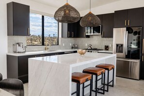 A modern kitchen with a large island, dark cabinetry, stainless steel appliances, and a view of the landscape. - Poco Cielo · Sauna, Cold Plunge, Hot Tub, Arcade (Joshua Tree)