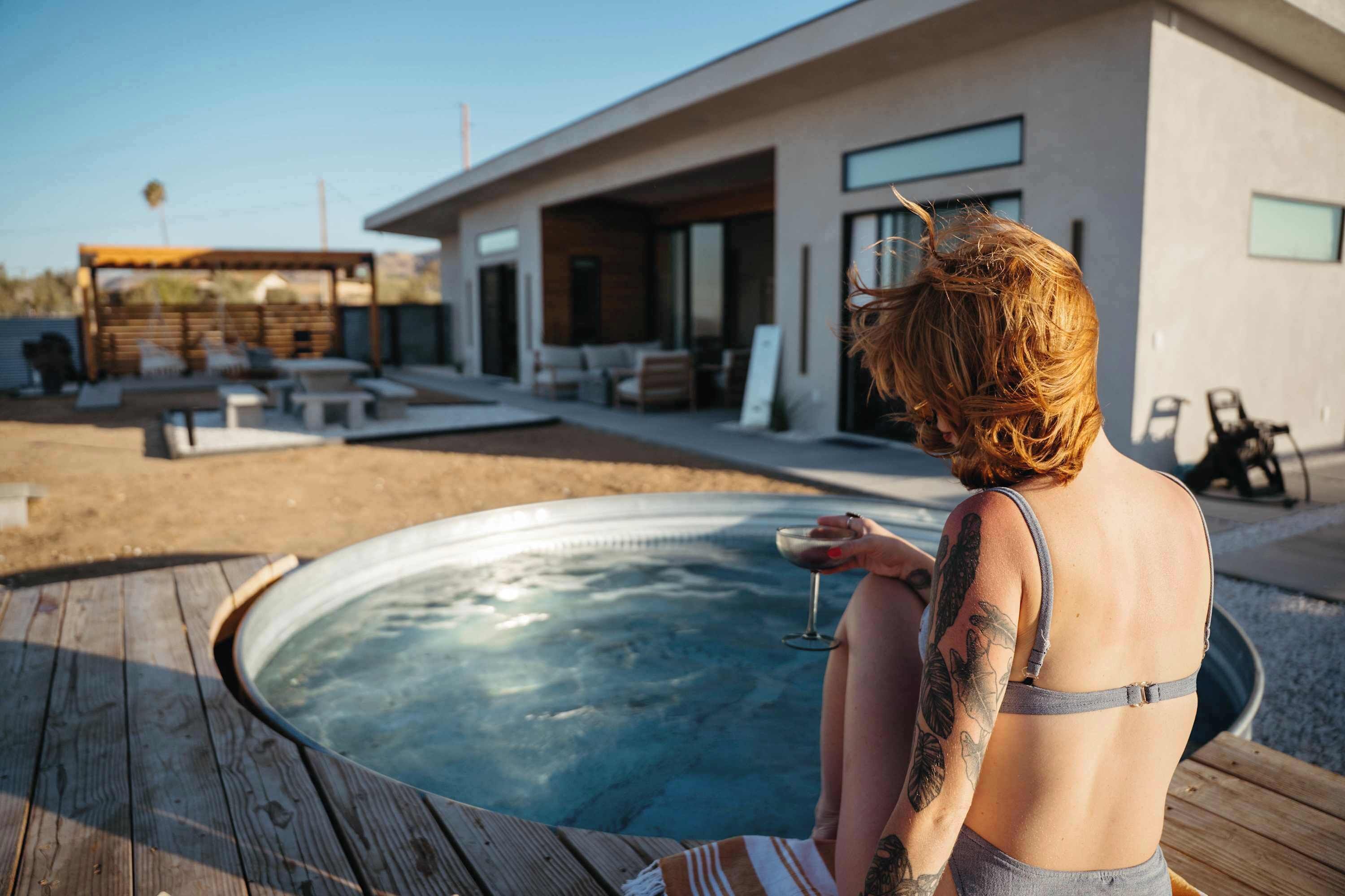 Une personne assise près d’un jacuzzi dans un cadre extérieur moderne, avec une piscine et un espace de détente.