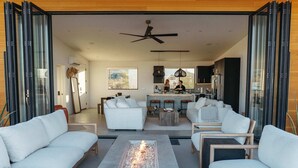 Ein modernes Wohnzimmer mit Kamin, weißen Sofas und einem Essbereich, im Hintergrund ist eine Küche zu sehen.