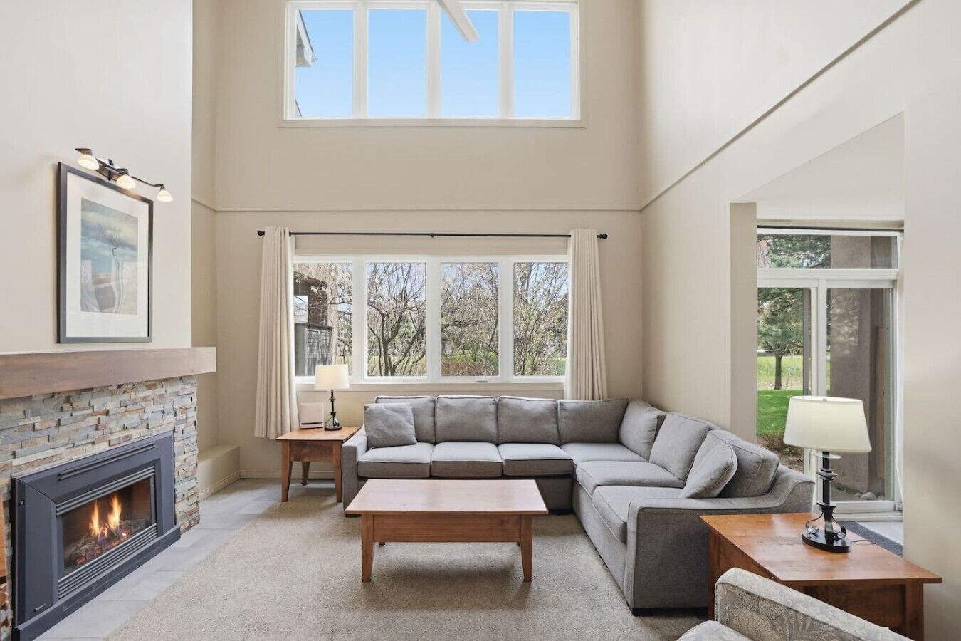 Un salon avec une cheminée, un canapé, une table basse et une fenêtre donnant sur des arbres.