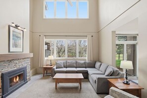 Ein Wohnzimmer mit Kamin, einer Couch, einem Couchtisch und einem Fenster mit Blick auf Bäume.