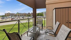 Un balcon avec une table et des chaises en verre, donnant sur un parking et des immeubles.