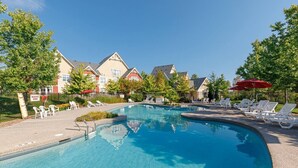 Ein Schwimmbecken mit Liegestühlen und Sonnenschirmen, umgeben von Gebäuden im traditionellen Baustil.