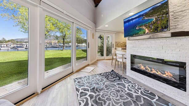 A modern living room with large windows, a fireplace, and a TV mounted on the wall. - Modern Studio Condo with Private Boat Dock (South Lake Tahoe)