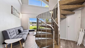 A modern interior with a curved staircase, a grey sofa, and a view of a green landscape through large windows. - Modern Studio Condo with Private Boat Dock (South Lake Tahoe)