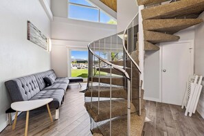 A modern interior with a curved staircase, a grey sofa, and a view of a green landscape through large windows. - Modern Studio Condo with Private Boat Dock (South Lake Tahoe)