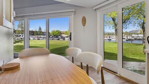 A dining area with a wooden table and chairs, large windows with a view of a park and boats. - Modern Studio Condo with Private Boat Dock (South Lake Tahoe)
