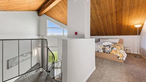 A bedroom with a bed, a window, a balcony with a railing, and a ceiling with wooden beams. - Modern Studio Condo with Private Boat Dock (South Lake Tahoe)