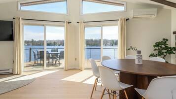 Una habitación con una mesa grande, sillas blancas, un televisor y vistas a un lago.