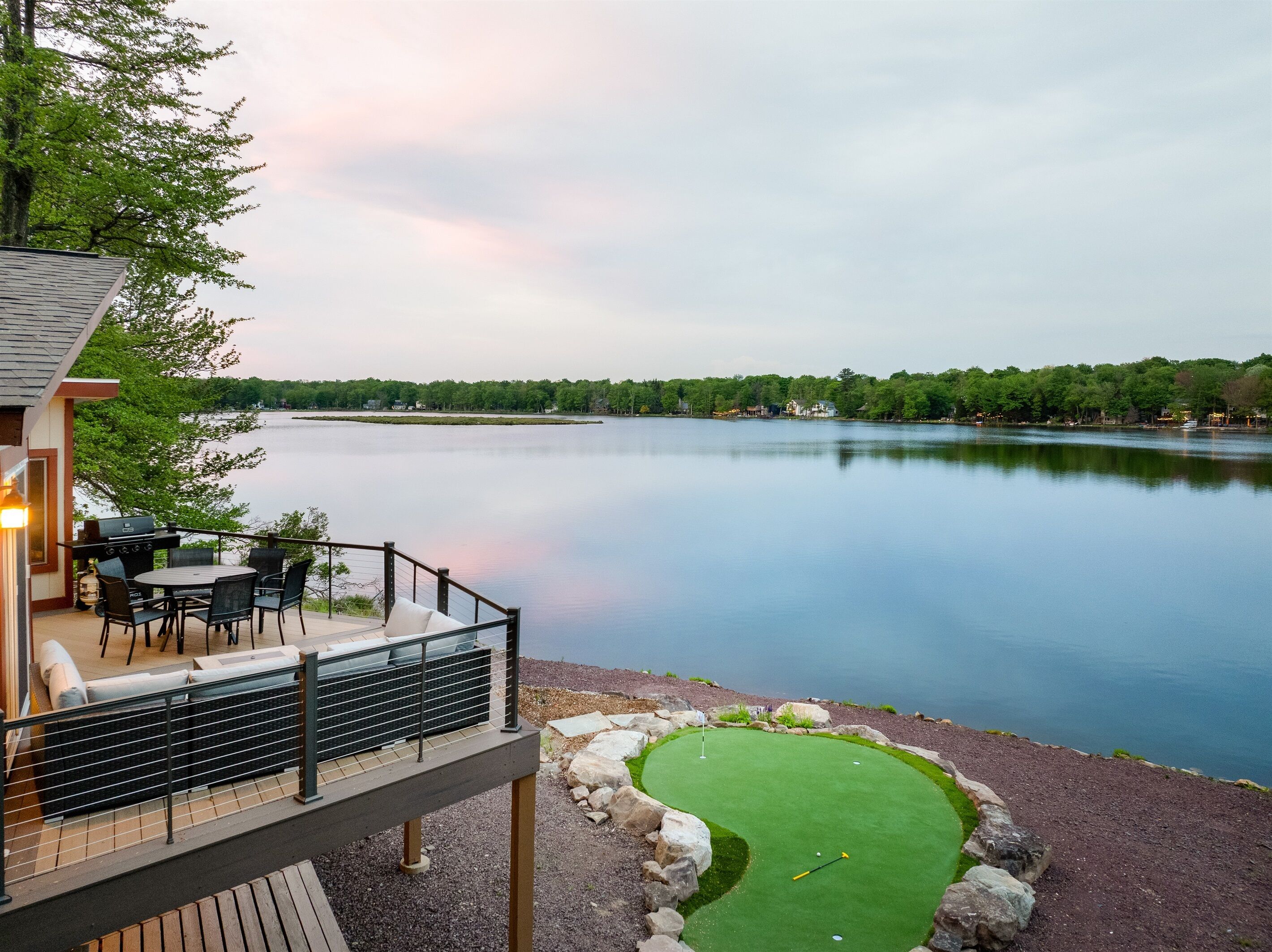 En ejendom ved søen med terrasse, udendørs møbler og en putting green.