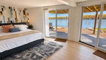 Un dormitorio con una cama grande, vista a un lago y puerta corrediza de vidrio que da a una terraza al aire libre.