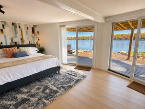 Een slaapkamer met een groot bed, uitzicht op een meer en een schuifdeur die leidt naar een terras.
