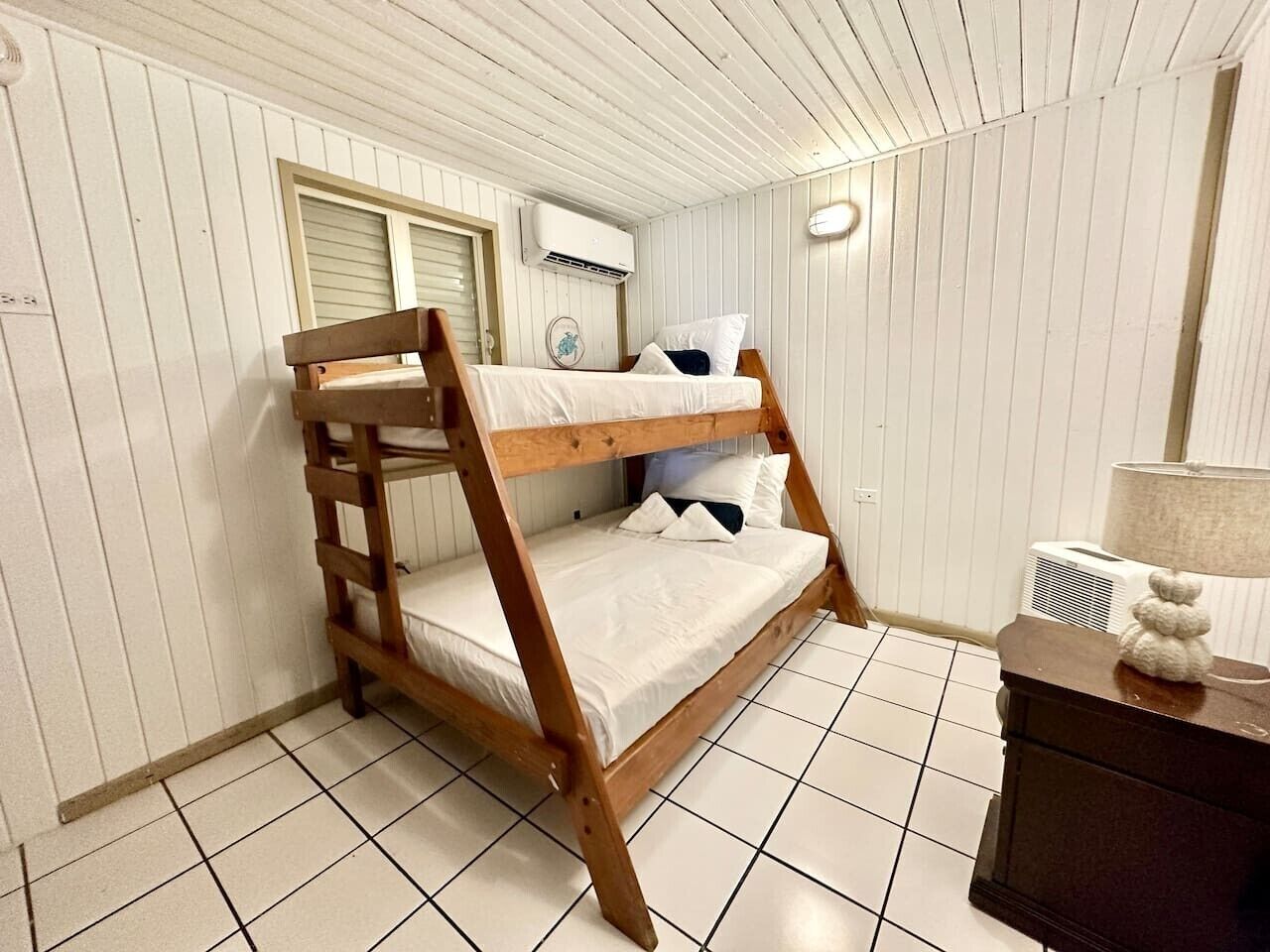 Un letto a castello in una stanza con pareti rivestite di bianco, pavimento piastrellato e un comodino con una lampada.