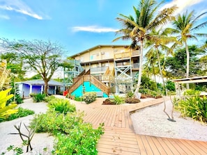 Een resort met een houten terras, palmbomen en een gebouw met meerdere balkons.