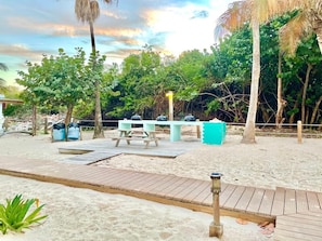Een zandstrand met een houten terras, picknicktafels en een barbecue.