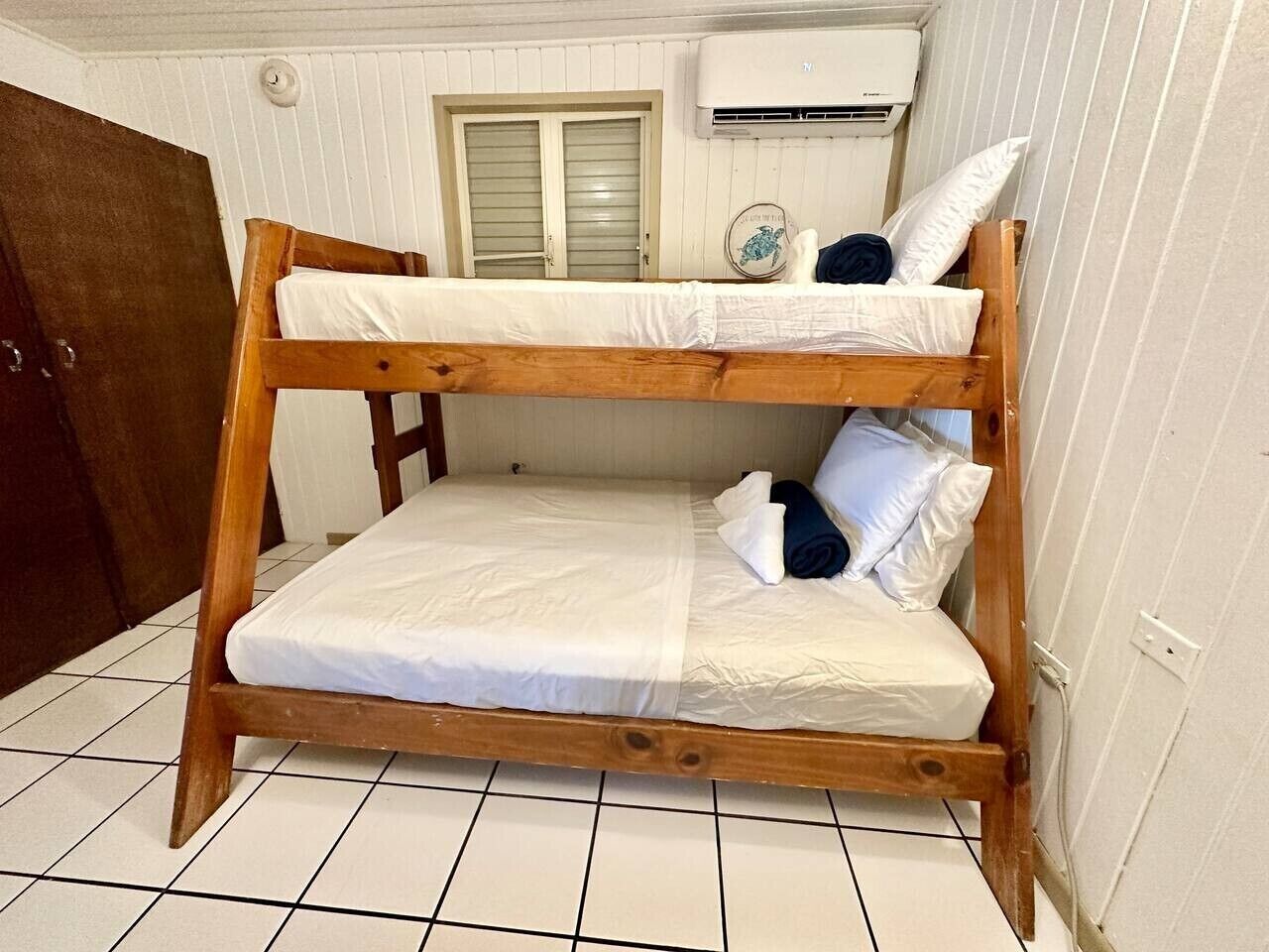 Una cama litera con ropa de cama blanca, estructura de madera y una ventana pequeña con contraventanas.