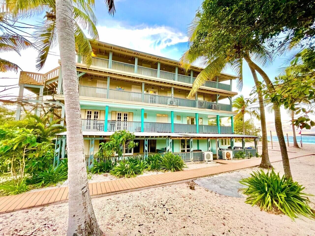 Un hotel de varios pisos con balcones, vista al mar y jardines tropicales.