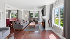 A modern living room with a fireplace, a television, and a dining area with red chairs.