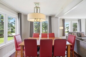Un comedor con mesa y sillas, un sofá y ventanas amplias con cortinas.