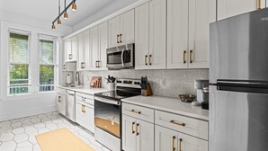 Una cocina moderna con armarios blancos, electrodomésticos de acero inoxidable y piso de baldosas hexagonales.