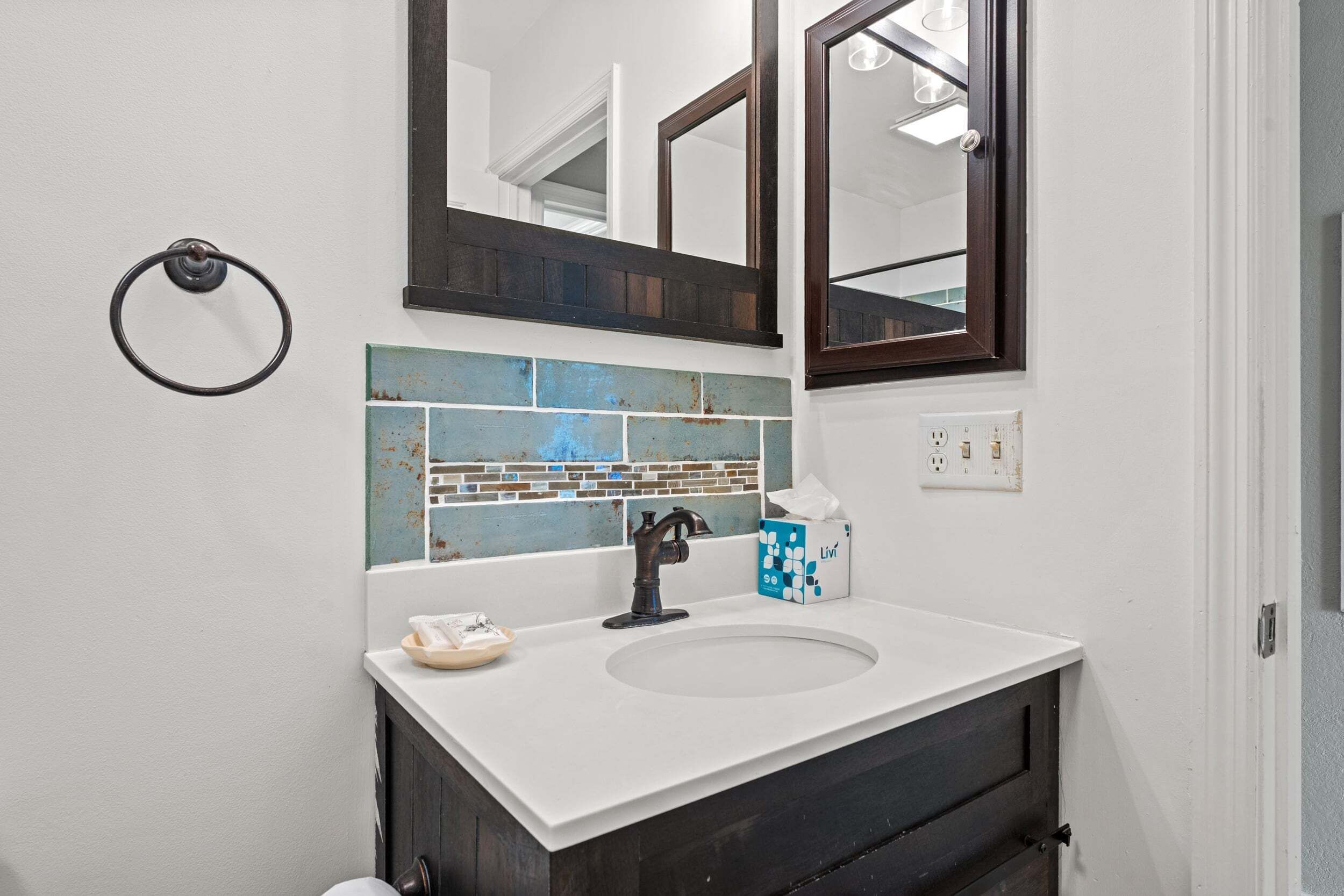 Une salle de bain avec un lavabo blanc, un meuble-lavabo foncé et un miroir au-dessus.