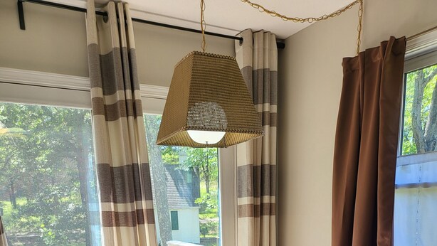 Une pièce avec une table en bois, deux tabourets noirs, une lampe suspendue et une vue sur la verdure à l’extérieur.