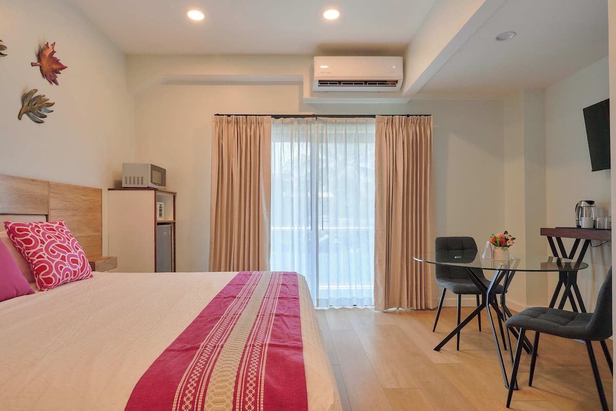 Una habitación de hotel con cama, escritorio con sillas, aire acondicionado y ventana con cortinas.