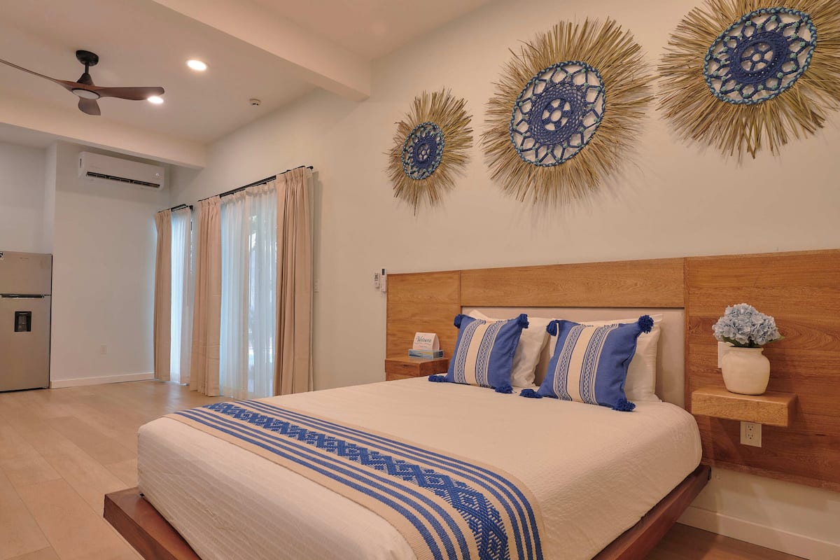Un dormitorio con cama, cortinas, ventilador de techo, decoración en la pared y una mesita de noche con un florero.