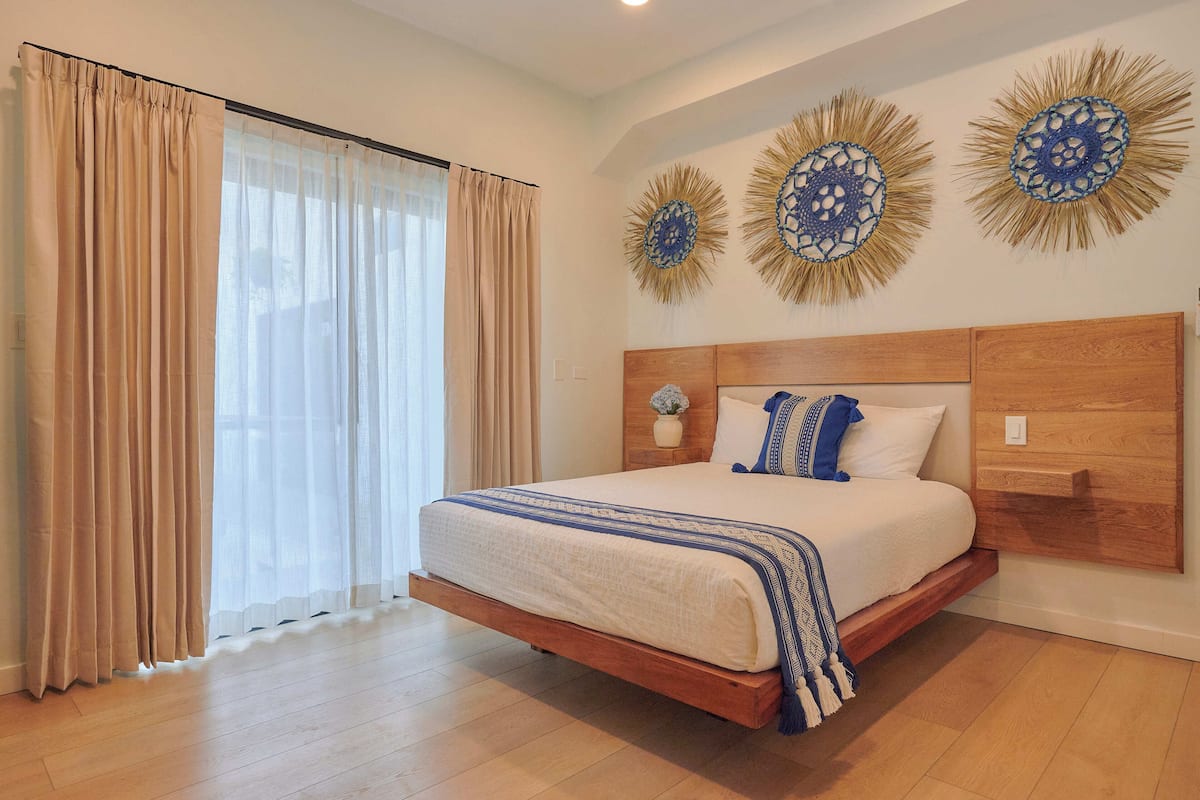 Un dormitorio con cama de madera, cortinas color beige y decoración mural.