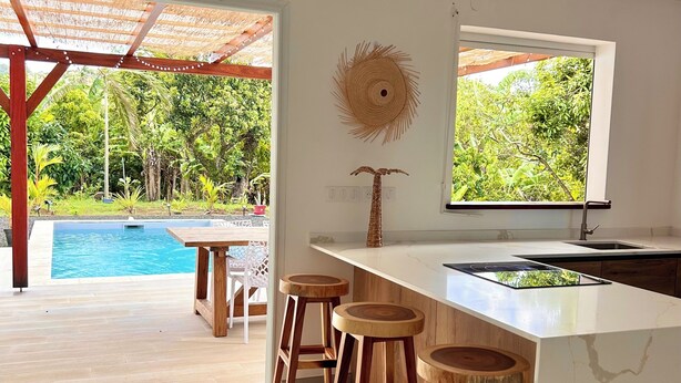 Eine moderne Küche mit Marmorarbeitsplatte, Holzbarhocker und Blick auf einen Swimmingpool.