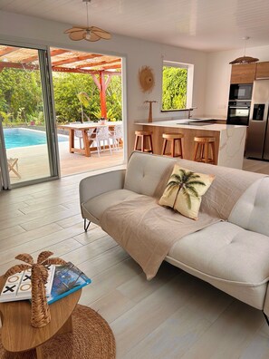 A modern living room with a sofa, a dining area, and a kitchen. - Casa Helena – Brand-New Villa – Private Pool &Tropical Garden – 6 P – Martinique (Saint-Esprit)