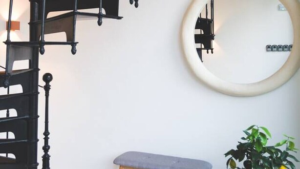 A staircase with a black railing, a round mirror on the wall, a bench, and a potted plant. - Violet ~ Romantische suite in Brugge (Brugge)