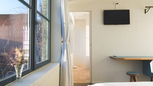 Una habitación de hotel con un ventanal grande, una cama, un escritorio y una televisión.
