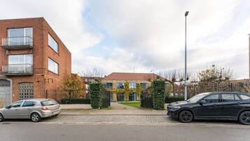 Een woonstraat met twee geparkeerde auto's aan de kant, een bakstenen gebouw met een balkon en een huis met een rood dak.